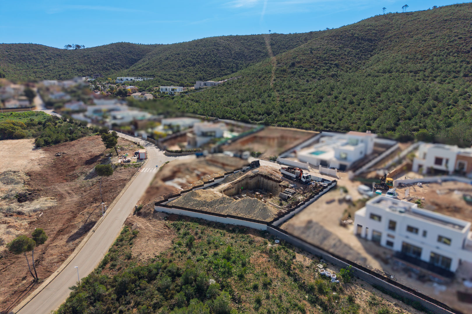 Vista aérea de la parcela en fase de excavación y cimentación, ubicada en la urbanización Valsol, rodeada de colinas verdes y villas modernas.