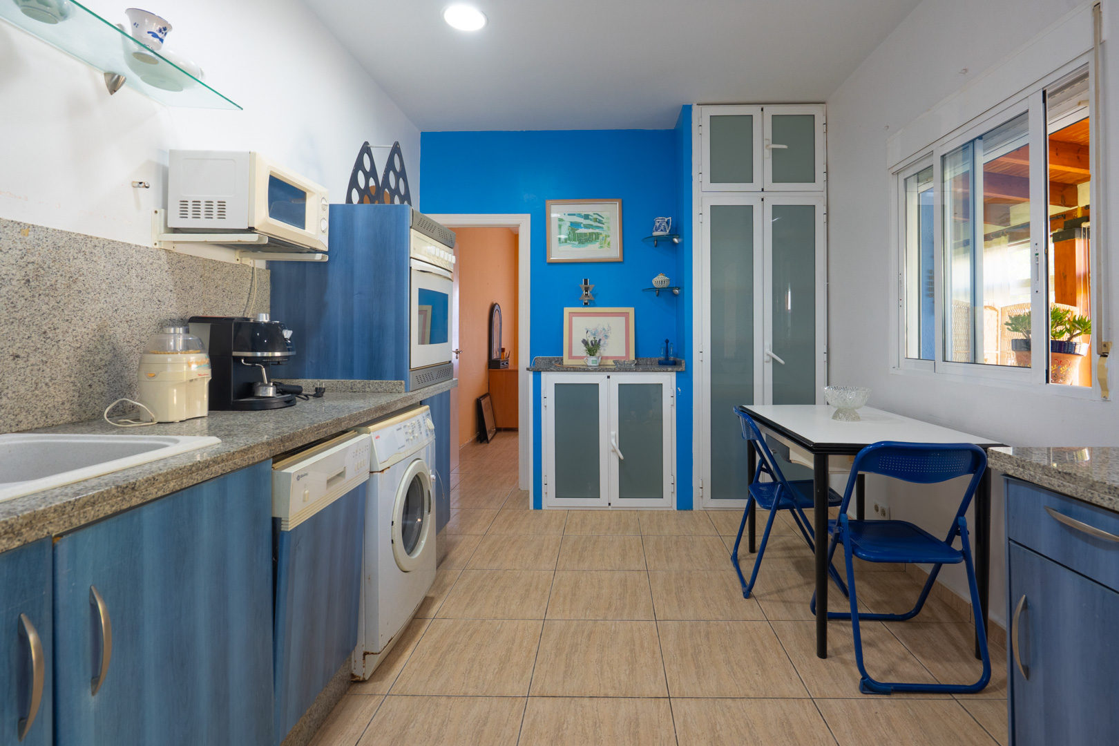 Cocina equipada con armarios de madera azul, encimeras de granito gris, zona de desayuno y electrodomésticos integrados bajo una iluminación empotrada.