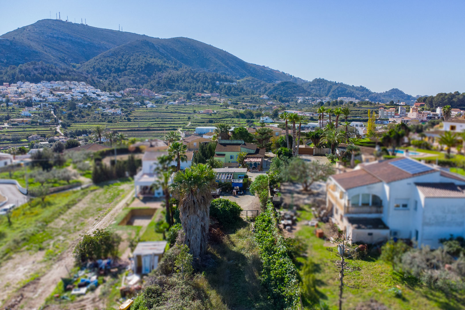 Vista aérea de la parcela rústica con la vivienda principal verde, la casa prefabricada y el entorno de bancales con vistas a la montaña.