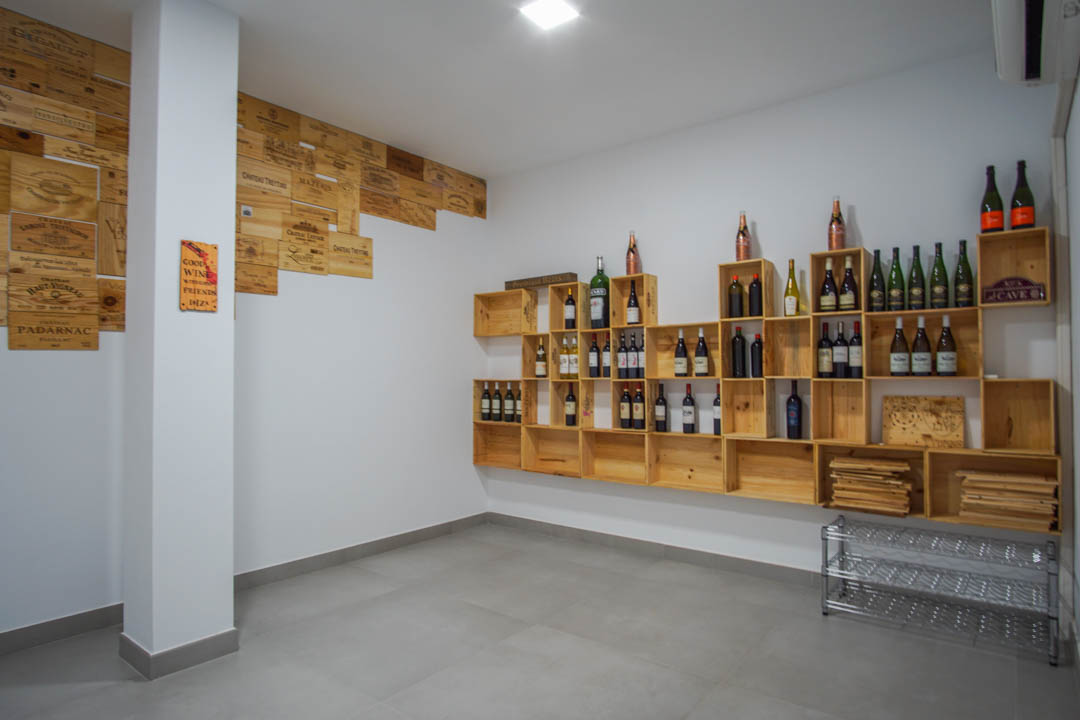 Bodega privada con estanterías modulares de madera y paneles decorativos de cajas de vino sobre paredes blancas y suelo de gres gris.