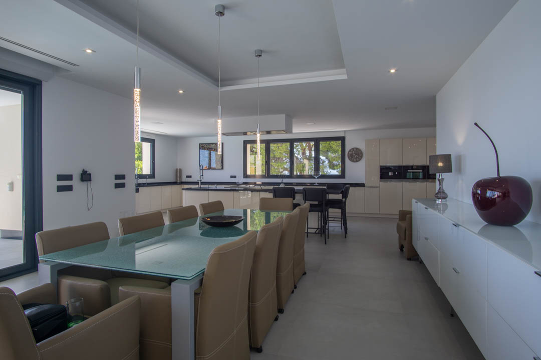 Comedor de diseño con mesa de cristal y sillas de cuero, integrado en una cocina abierta con encimeras oscuras e iluminación empotrada.