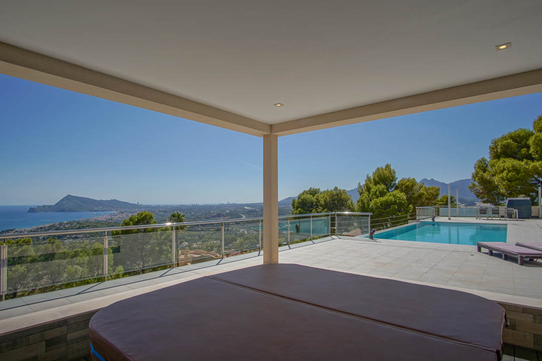 Terraza cubierta con jacuzzi, piscina exterior y vistas panorámicas a la bahía de Altea y Benidorm, delimitada por barandillas de cristal y acero.