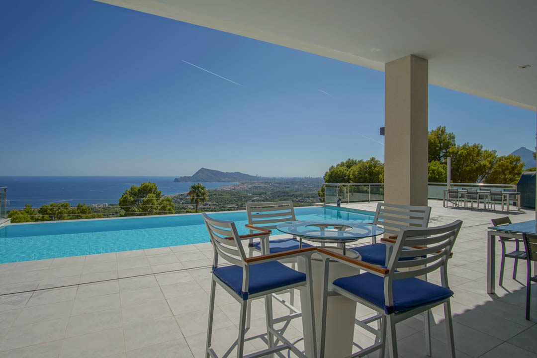 Terraza principal con piscina infinita y vistas panorámicas a la bahía de Altea. Incluye zona de estar con mobiliario moderno y suelos de gres porcelánico claro.