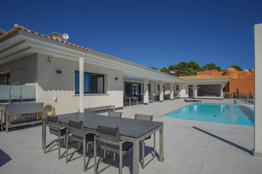 Terraza principal de 240m2 con suelos cerámicos grises, piscina de 10x4m y zona de comedor exterior junto a una cocina de verano equipada con fregadero industrial.