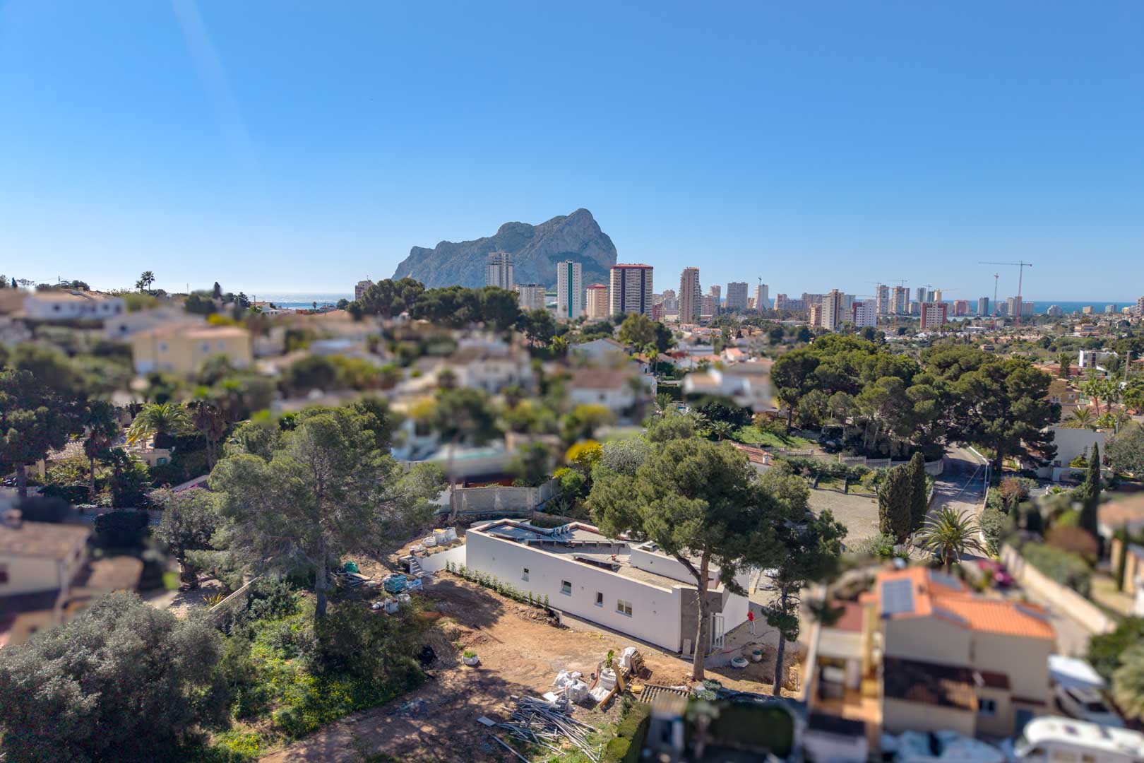 Vista aérea de la villa minimalista en construcción, resaltando su diseño de una planta y la ubicación privilegiada con vistas al Peñón de Ifach y al entorno urbano de Calpe.