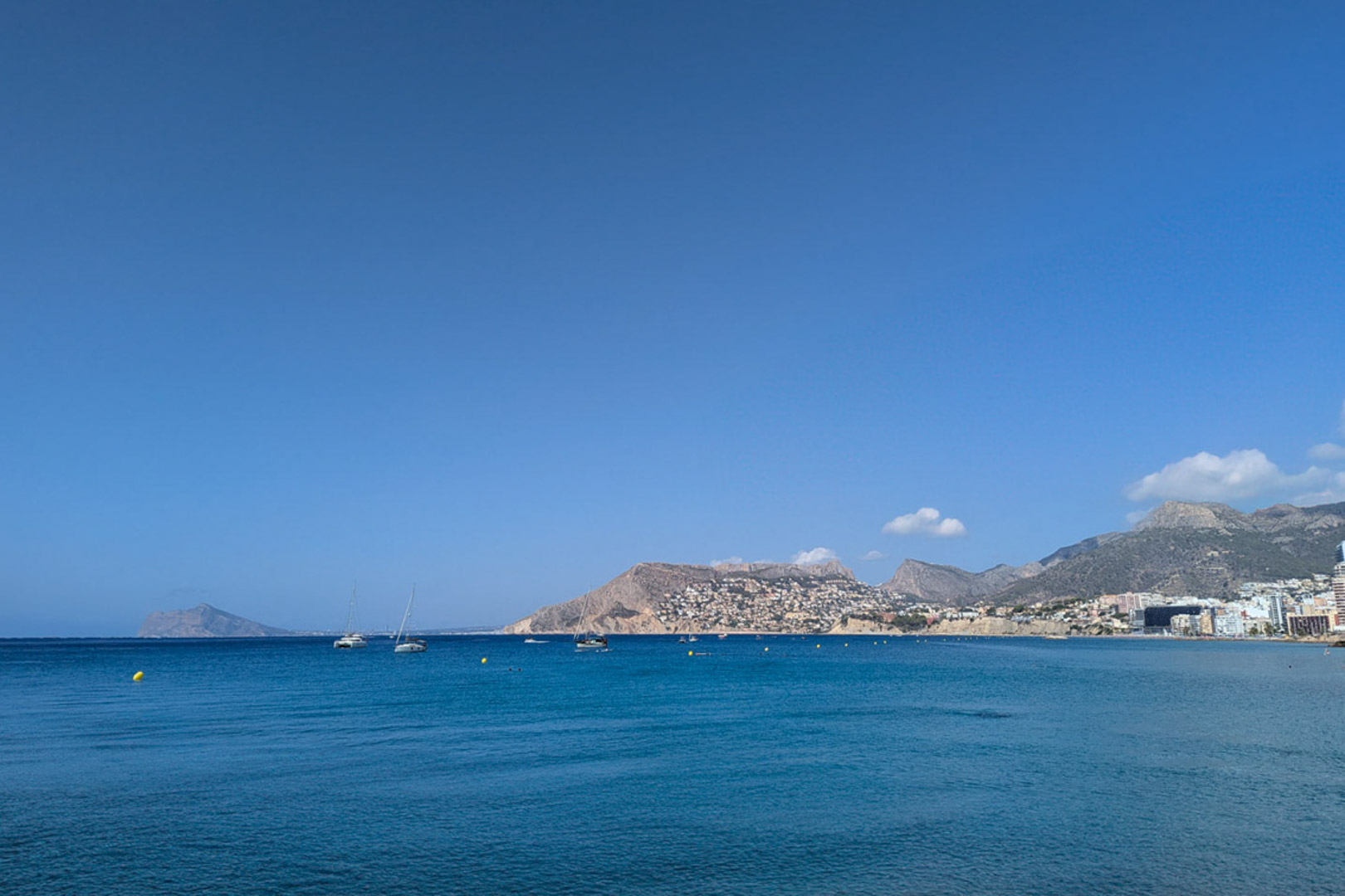 Vista panorámica del mar Mediterráneo desde la costa de Calpe, mostrando embarcaciones de recreo y el perfil montañoso de la zona bajo un cielo despejado.