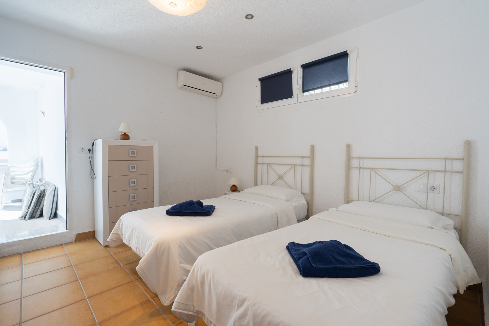 Dormitorio con dos camas individuales, suelos de terracota y aire acondicionado. Incluye acceso directo a la terraza y abundante luz natural.
