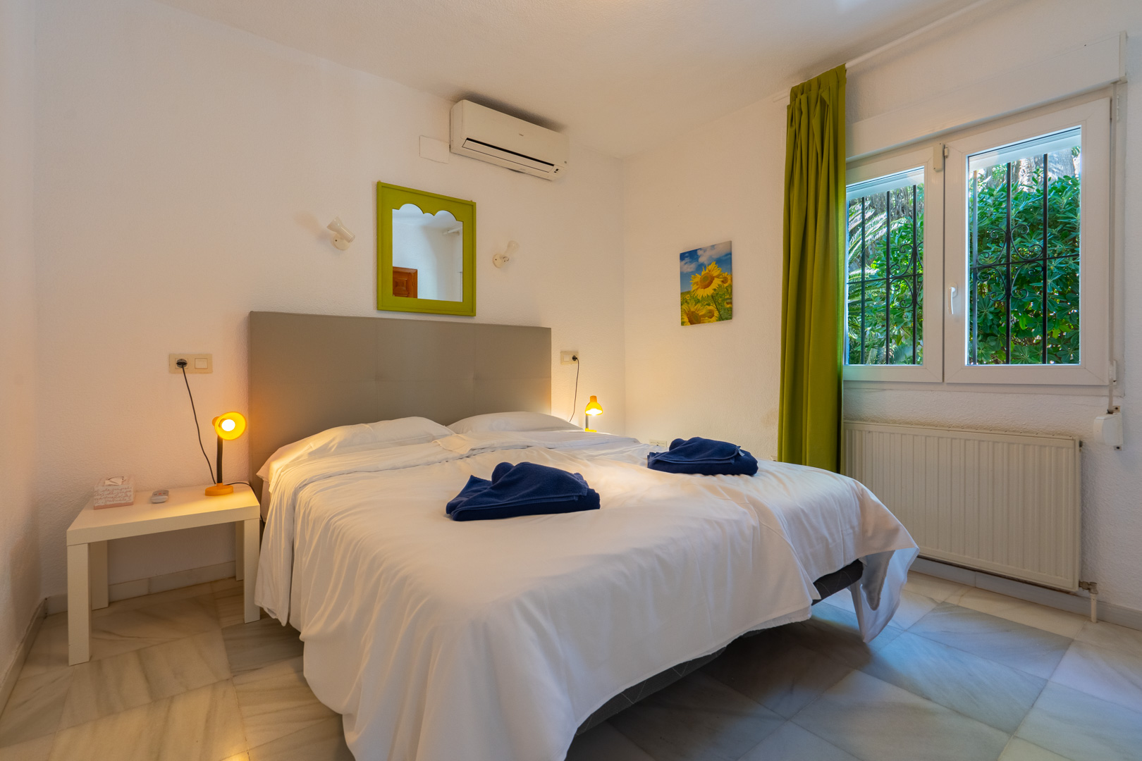 Dormitorio con suelos de mármol, aire acondicionado y calefacción. Incluye una ventana con rejas de seguridad, cortinas verdes y un espejo decorativo a juego.