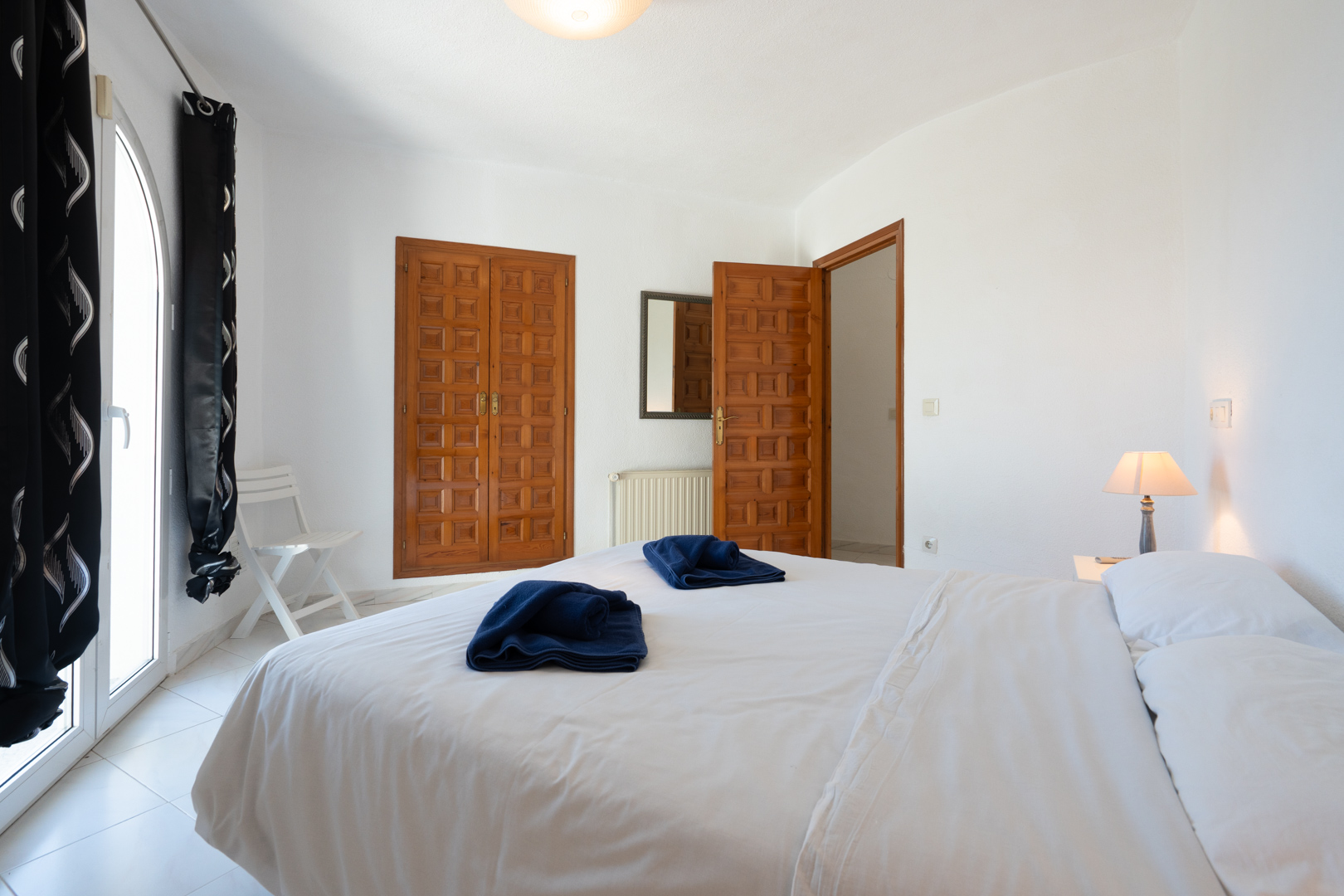 Dormitorio luminoso con armarios empotrados de madera tradicional, acceso directo al exterior mediante puerta acristalada de arco y suelos cerámicos claros.