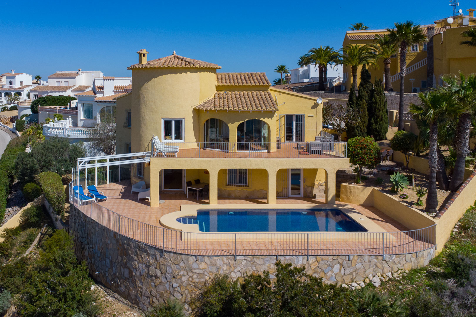 Fachada de la villa con piscina privada, amplias terrazas de terracota en dos niveles y un robusto muro de contención construido en piedra natural.