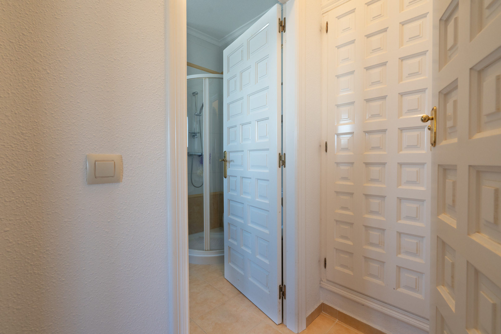 Pasillo con armarios empotrados blancos de diseño tradicional y acceso a un baño con ducha de esquina y mampara de cristal curva.