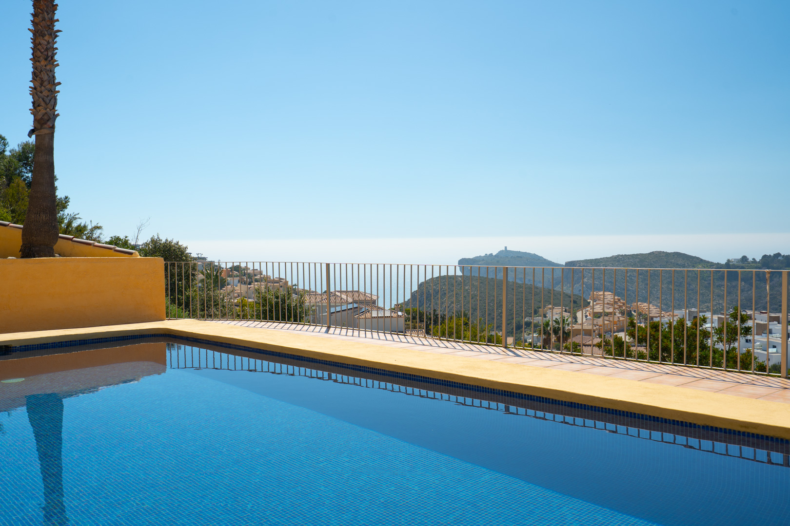 Piscina de gresite azul con vistas panorámicas al mar y al Cap d’Or en Moraira, integrada en una terraza con barandilla metálica de seguridad.