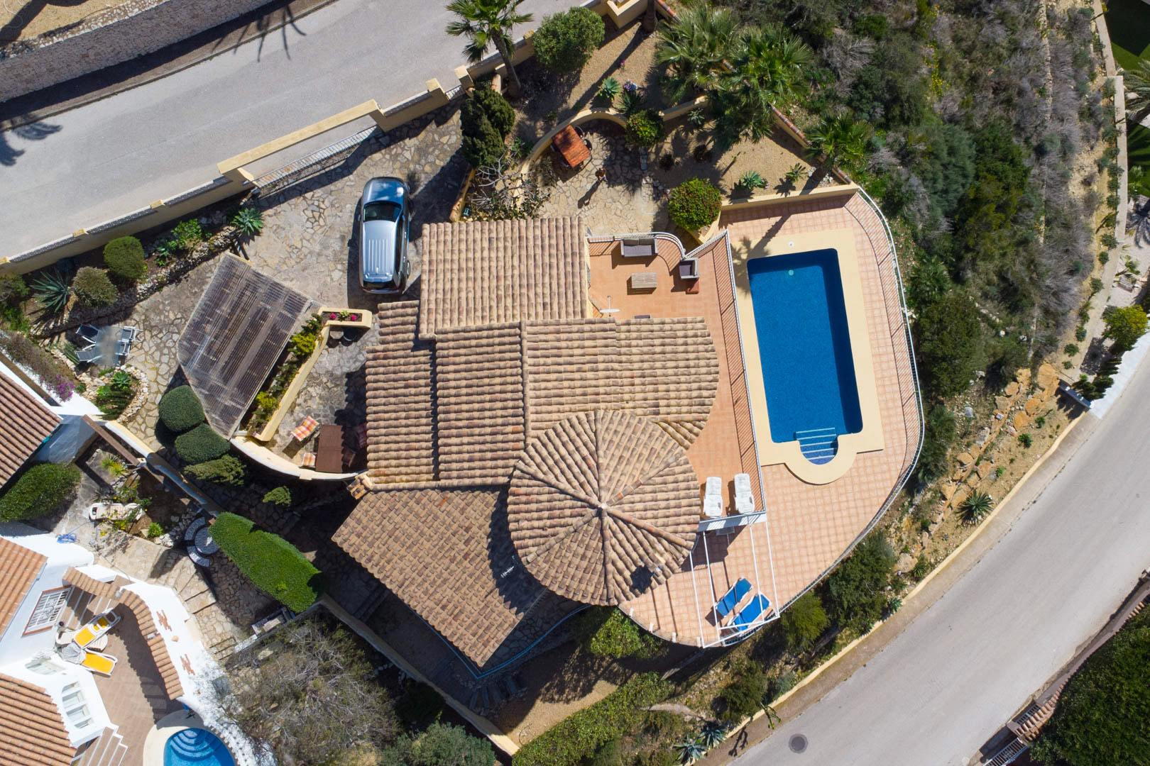 Vista aérea que muestra la planta de la villa, con su tejado de teja tradicional, la piscina rectangular con amplia terraza y la zona de aparcamiento con carport.