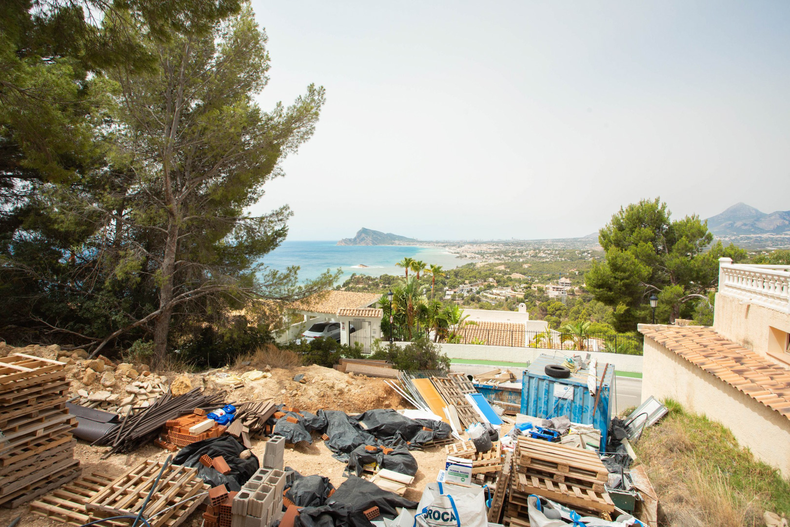 Vista elevada desde la parcela en Altea Hills, mostrando materiales de obra y un panorama despejado hacia el mar Mediterráneo y la costa de Altea.
