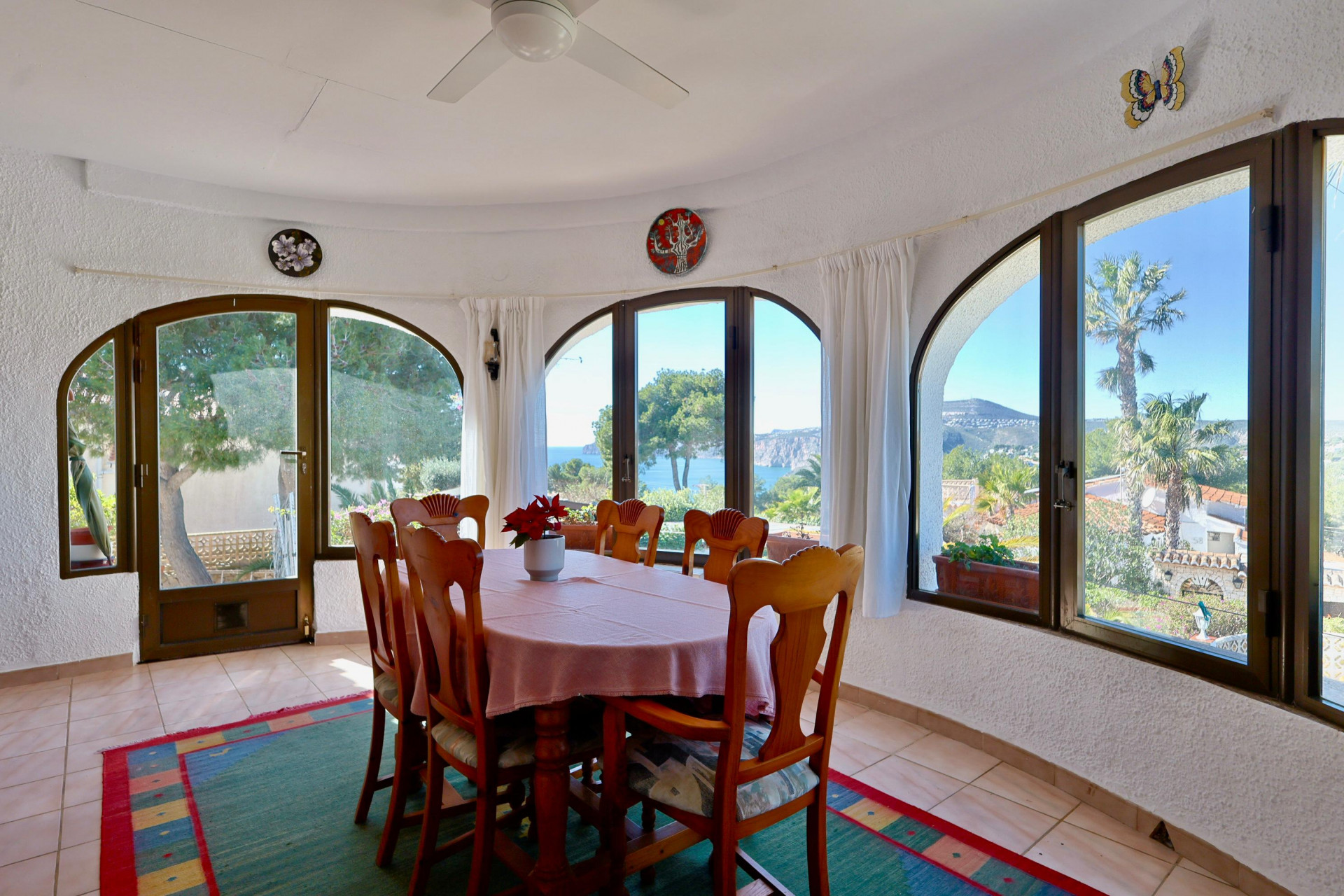Comedor luminoso con vistas al mar, rodeado de ventanas arqueadas y decoración rústica.