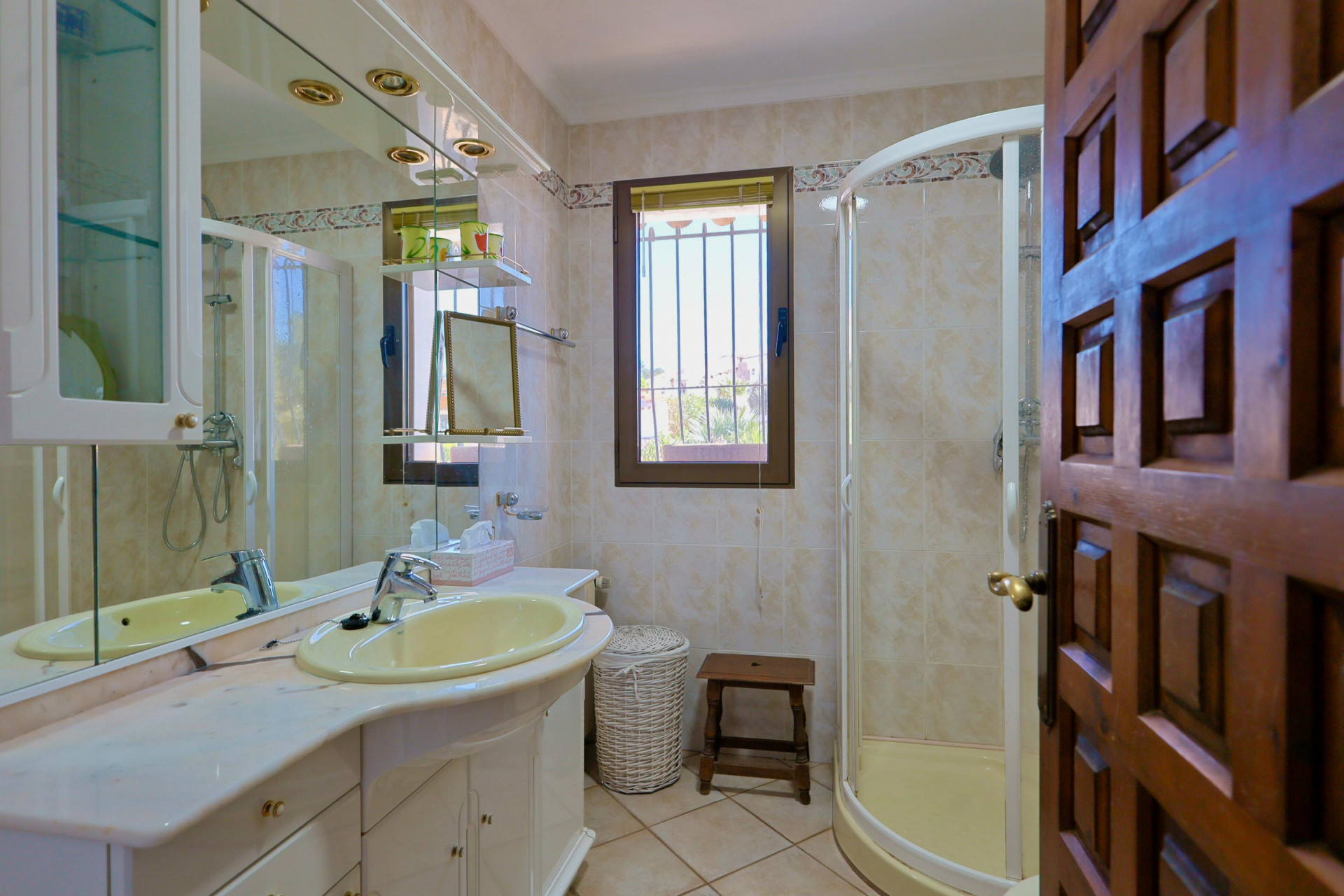 Detalle de baño con lavabo amarillo, ducha esquinera y puerta de madera tallada.
