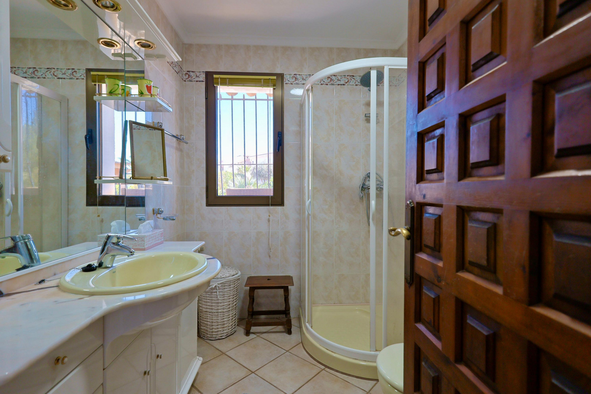 Detalle del baño con lavabo amarillo, ducha esquinera y puerta de madera tallada.