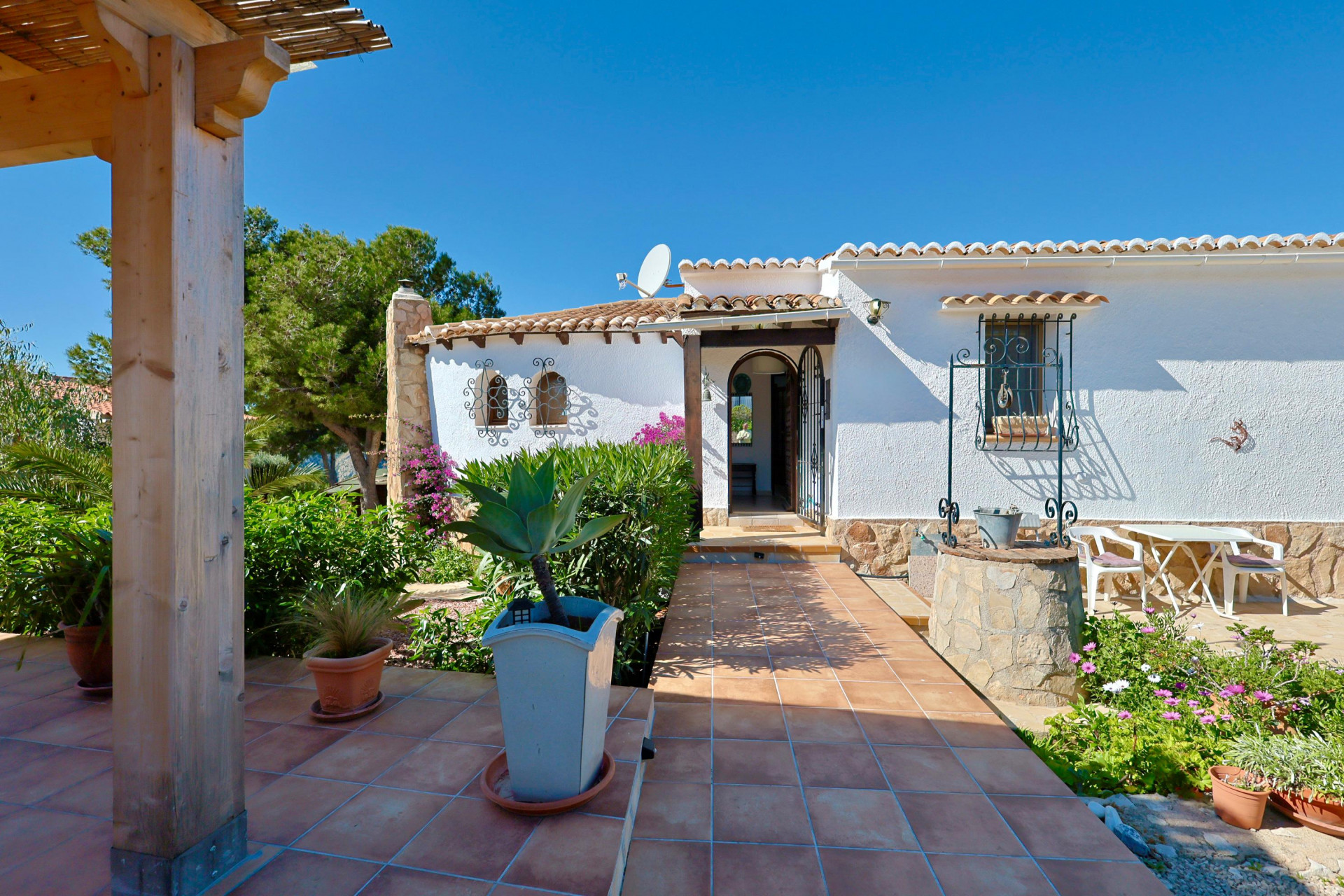 Entrada de la villa con pozo decorativo, jardín y terraza con suelo de baldosas.