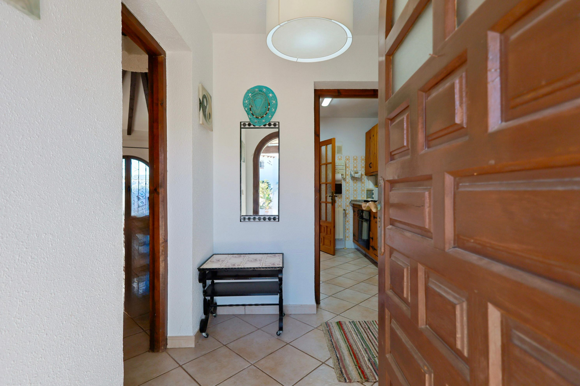 Entrada luminosa con espejo decorativo y puerta de madera maciza entreabierta a la cocina.