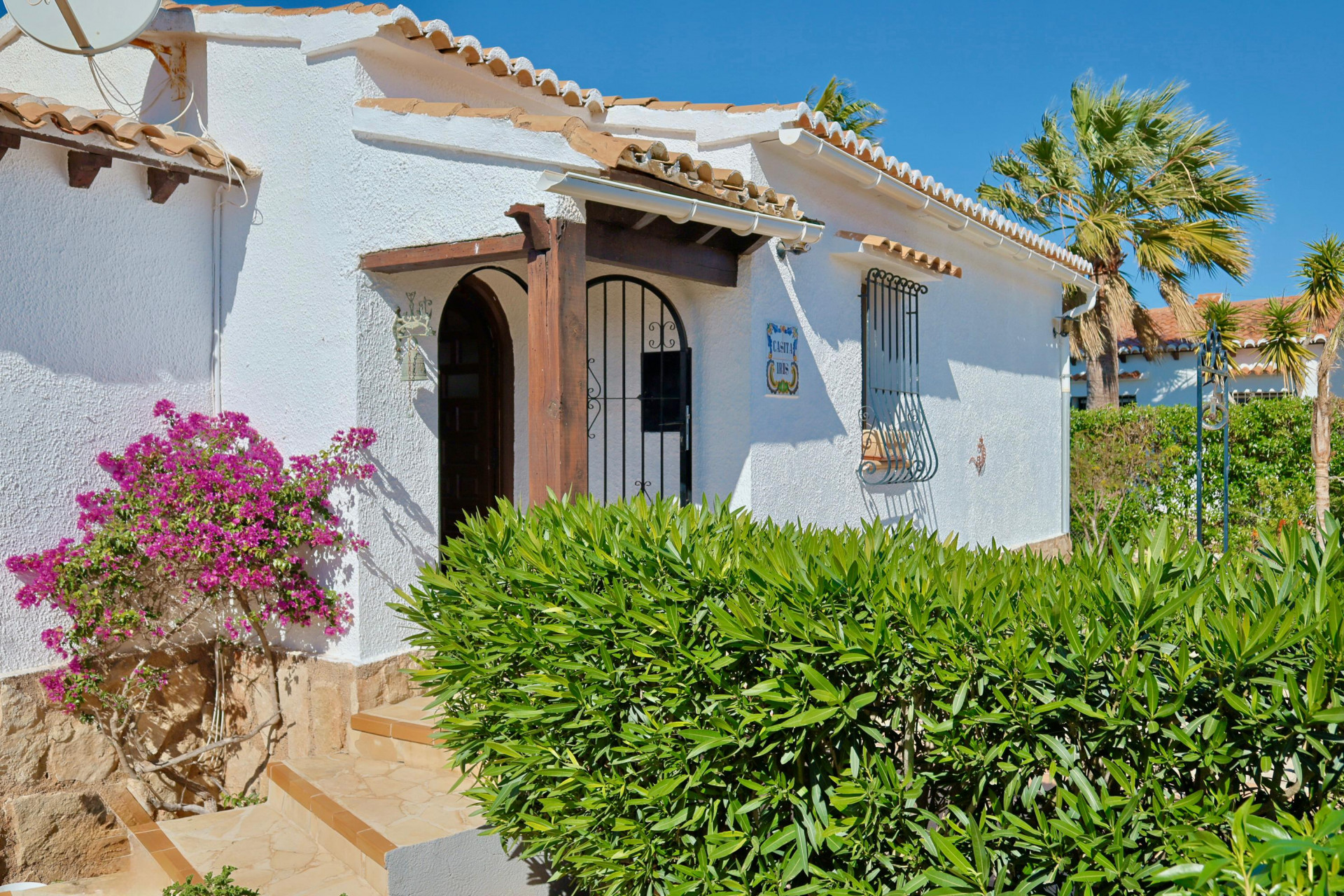 Fachada de villa mediterránea con buganvilla y detalles de madera.