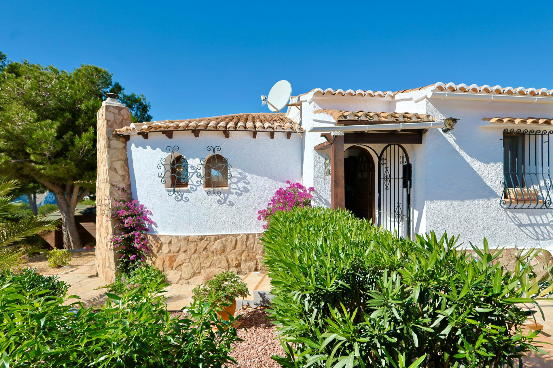 Fachada de villa mediterránea con detalles de piedra, tejas y rejas ornamentales.