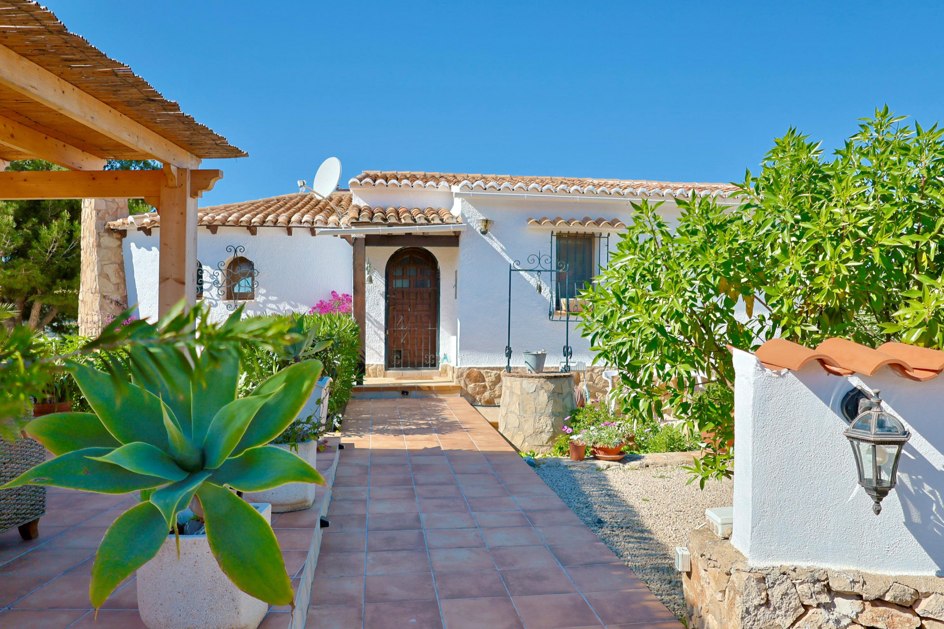Vista de la entrada principal con pozo de piedra y camino de baldosas.