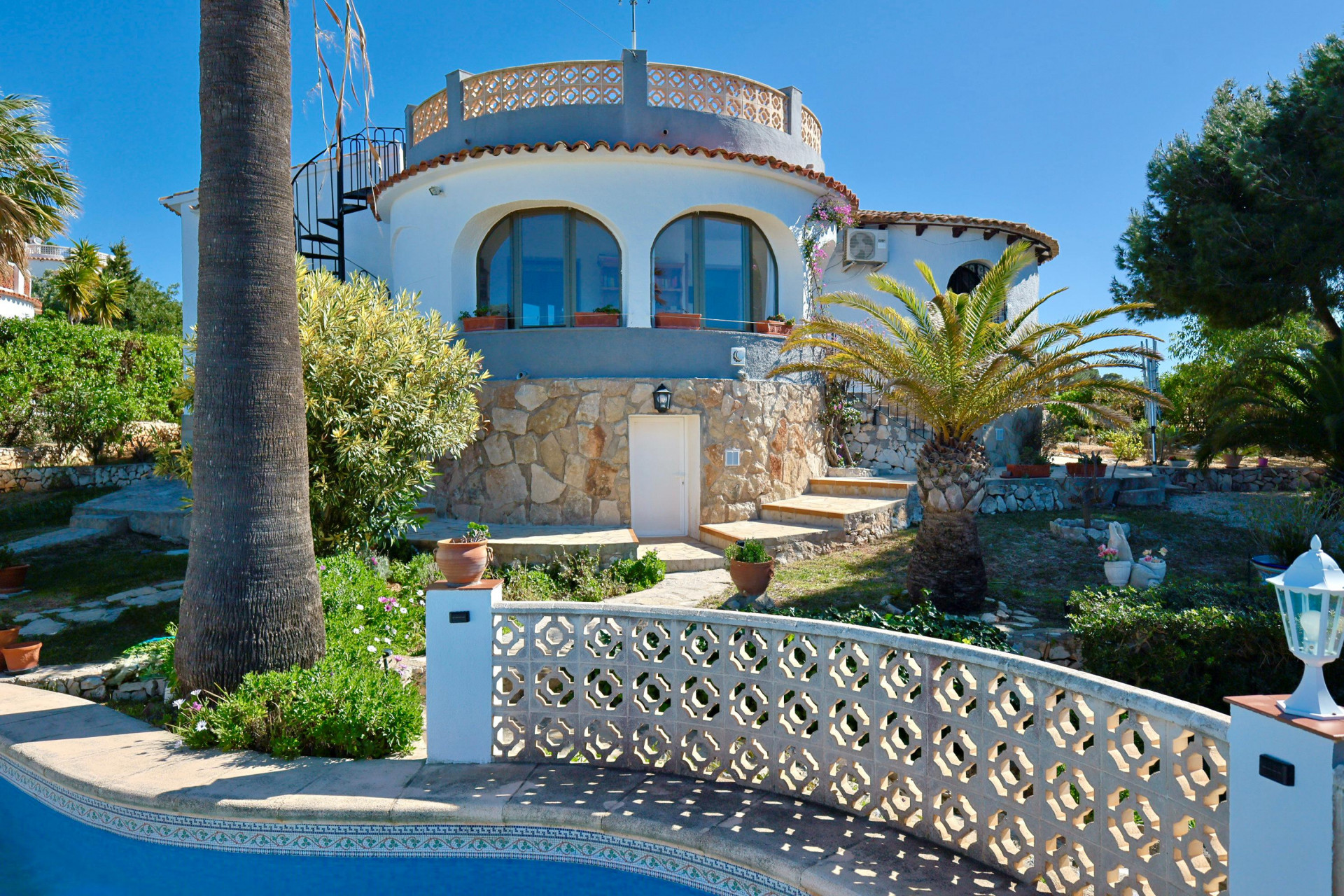 Vista exterior de la villa con piscina y fachada de piedra, rodeada de jardines mediterráneos.