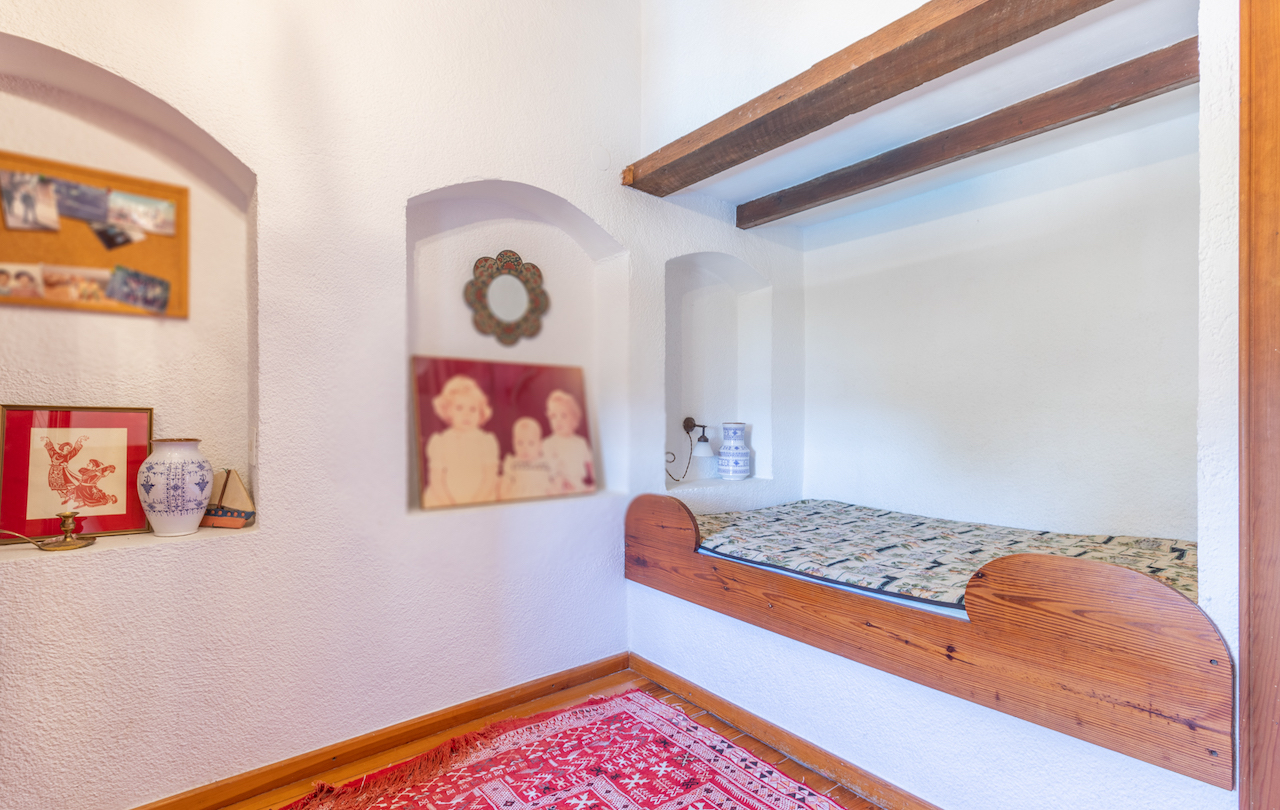 Dormitorio rústico con cama encastrada en madera, vigas vistas y nichos decorativos integrados en paredes blancas de estilo tradicional valenciano.