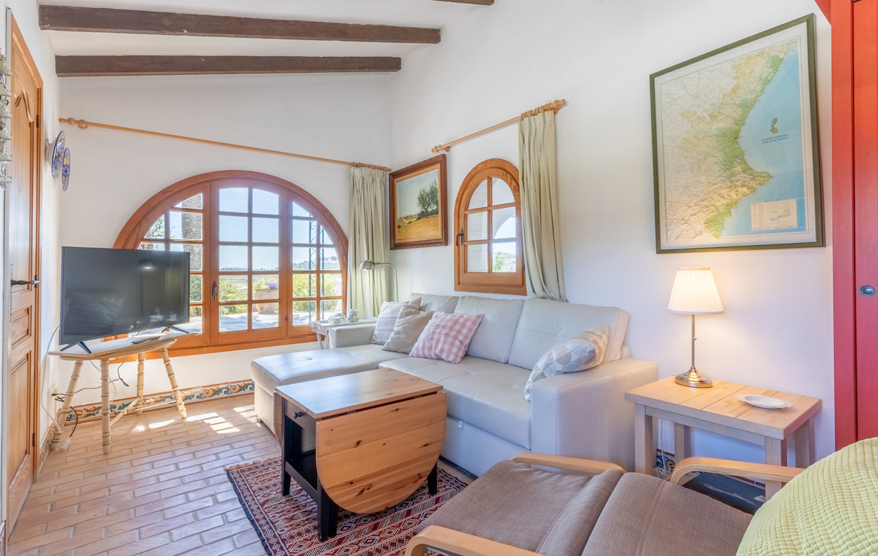 Salón rústico con vigas de madera vista, suelo de barro cocido y ventanales de arco que ofrecen luz natural y vistas al exterior de la finca.