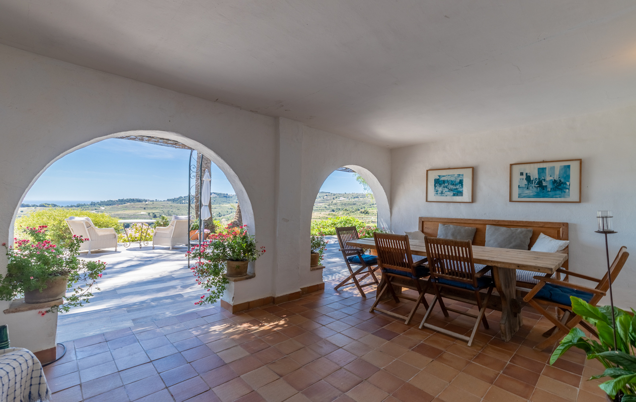 Terraza cubierta con arcos tradicionales, suelo de barro y zona de comedor rústica. Ofrece vistas despejadas a los viñedos y al mar Mediterráneo desde su posición elevada.