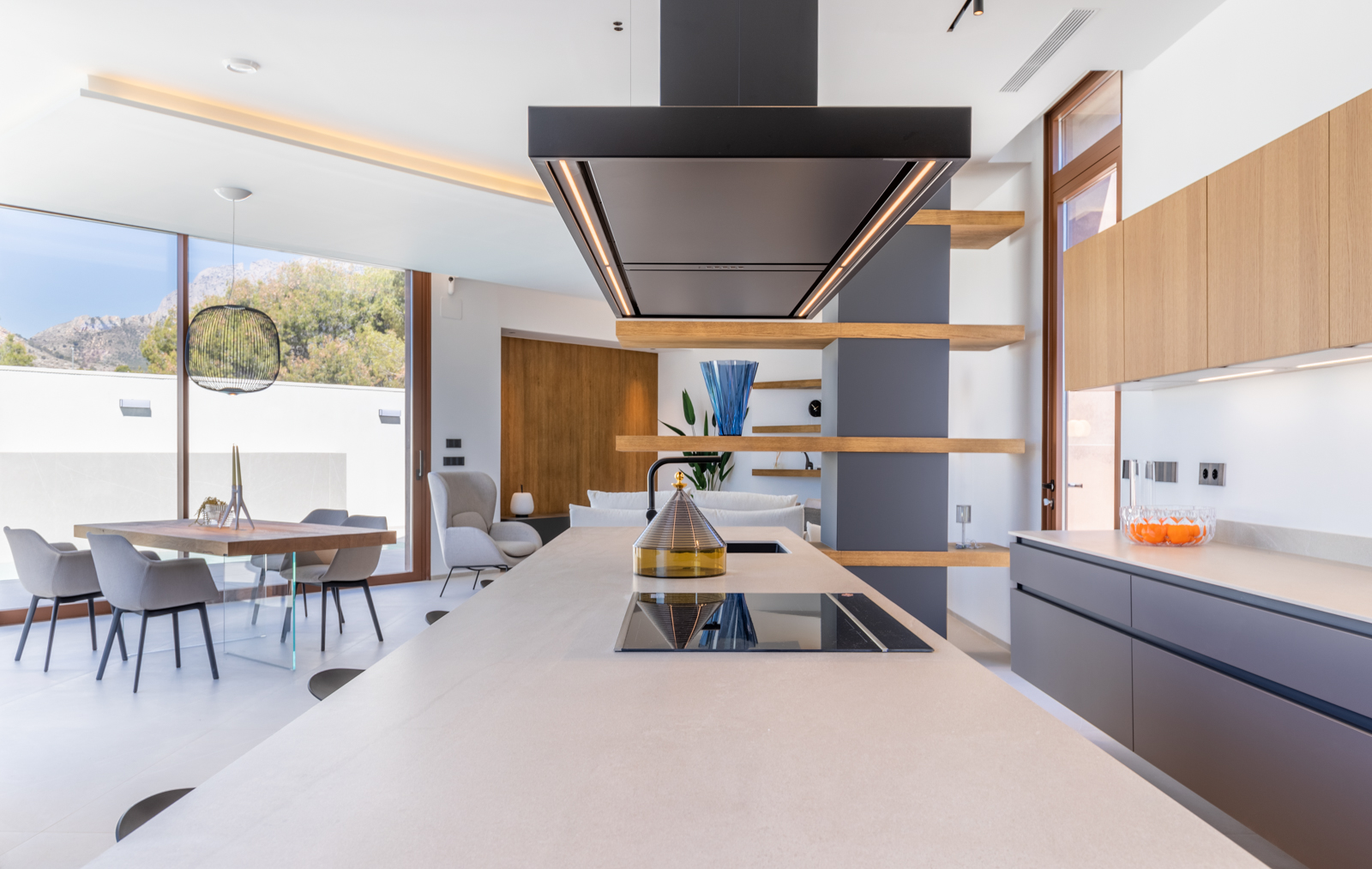 Detalle de la cocina moderna con isla central, campana extractora negra y estanterías de madera vista.