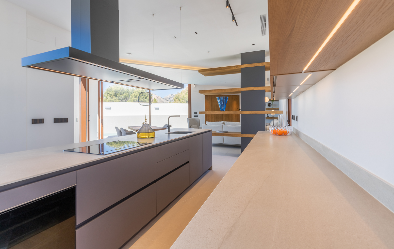 Detalle de la cocina moderna con isla gris, encimera beige y estantes de madera iluminados.