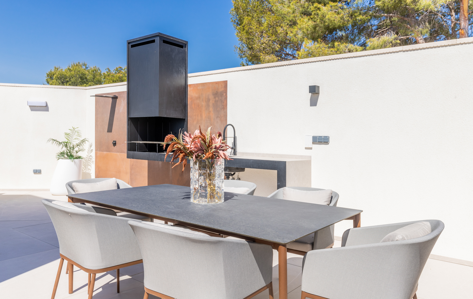 Detalle de la zona de barbacoa exterior con mesa de comedor y sillas grises en La Nucía.