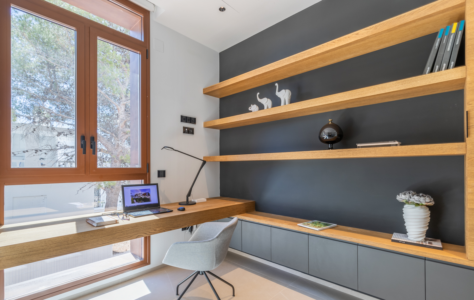 Oficina en casa con estanterías de madera clara y escritorio integrado junto a la ventana.