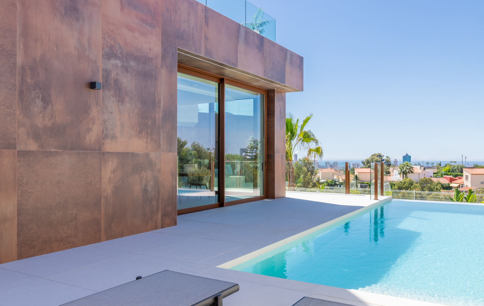 Vista de la piscina infinita con fachada de paneles color óxido y vistas panorámicas de la ciudad.