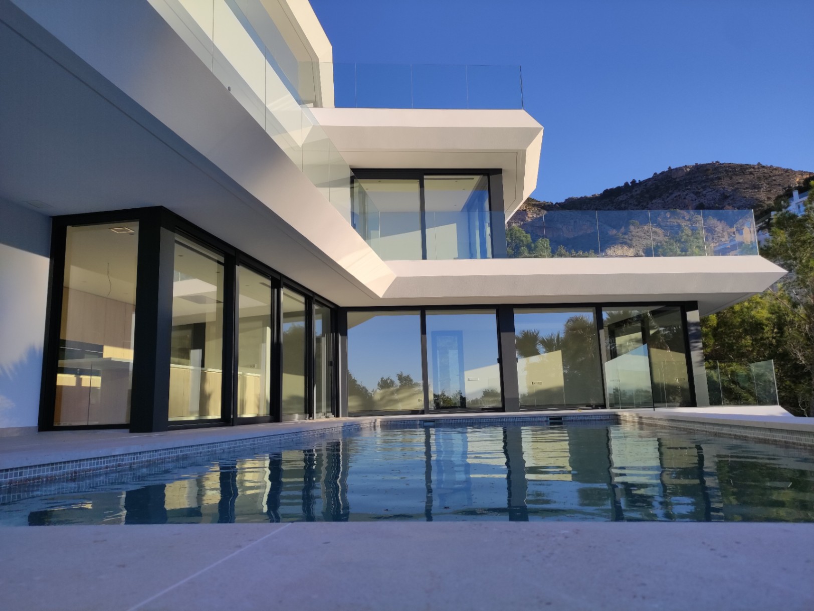 Fachada moderna con amplios ventanales de carpintería negra y piscina infinita que refleja la arquitectura geométrica bajo el cielo despejado de Altea Hills.