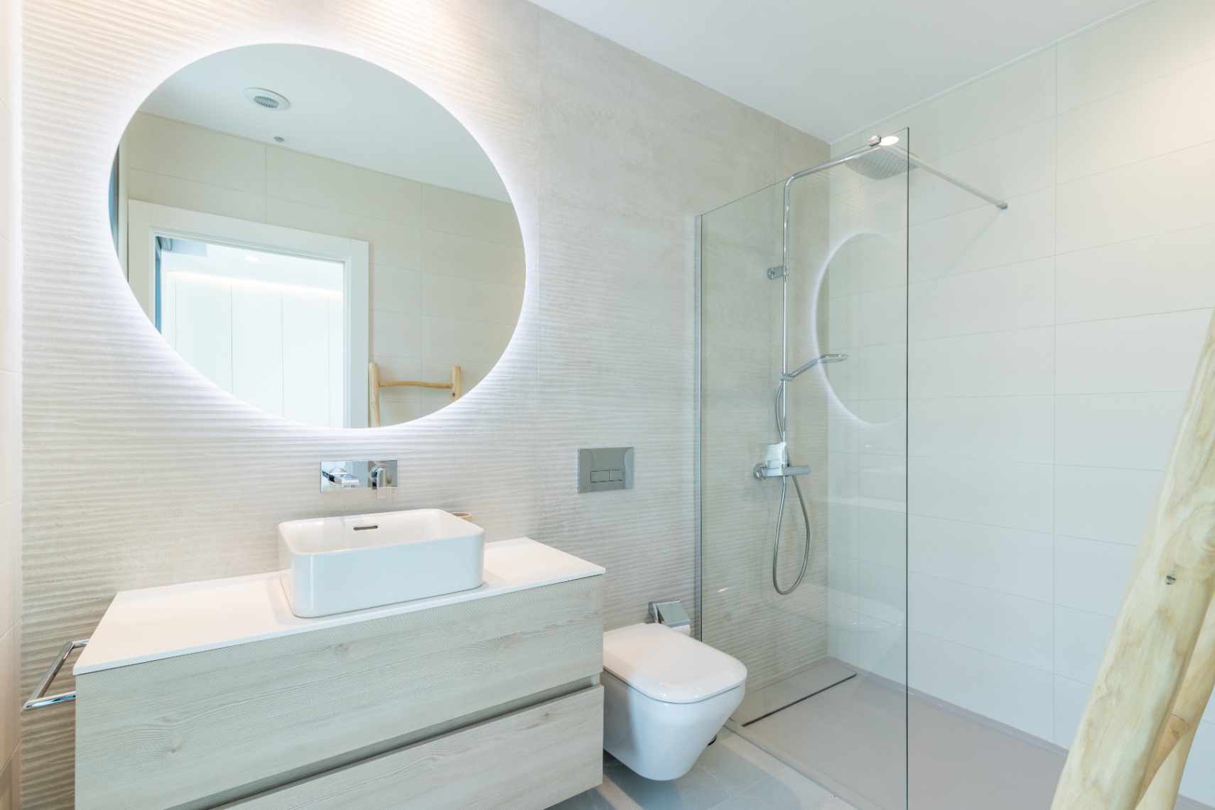 Baño moderno con lavabo cuadrado, espejo retroiluminado y ducha con mampara de cristal.