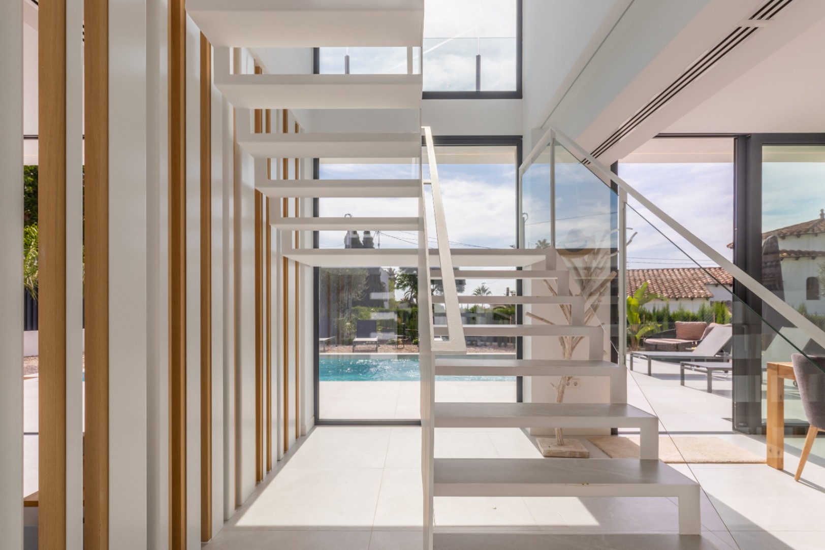 Escalera flotante blanca con barandilla de cristal y listones verticales de madera clara.