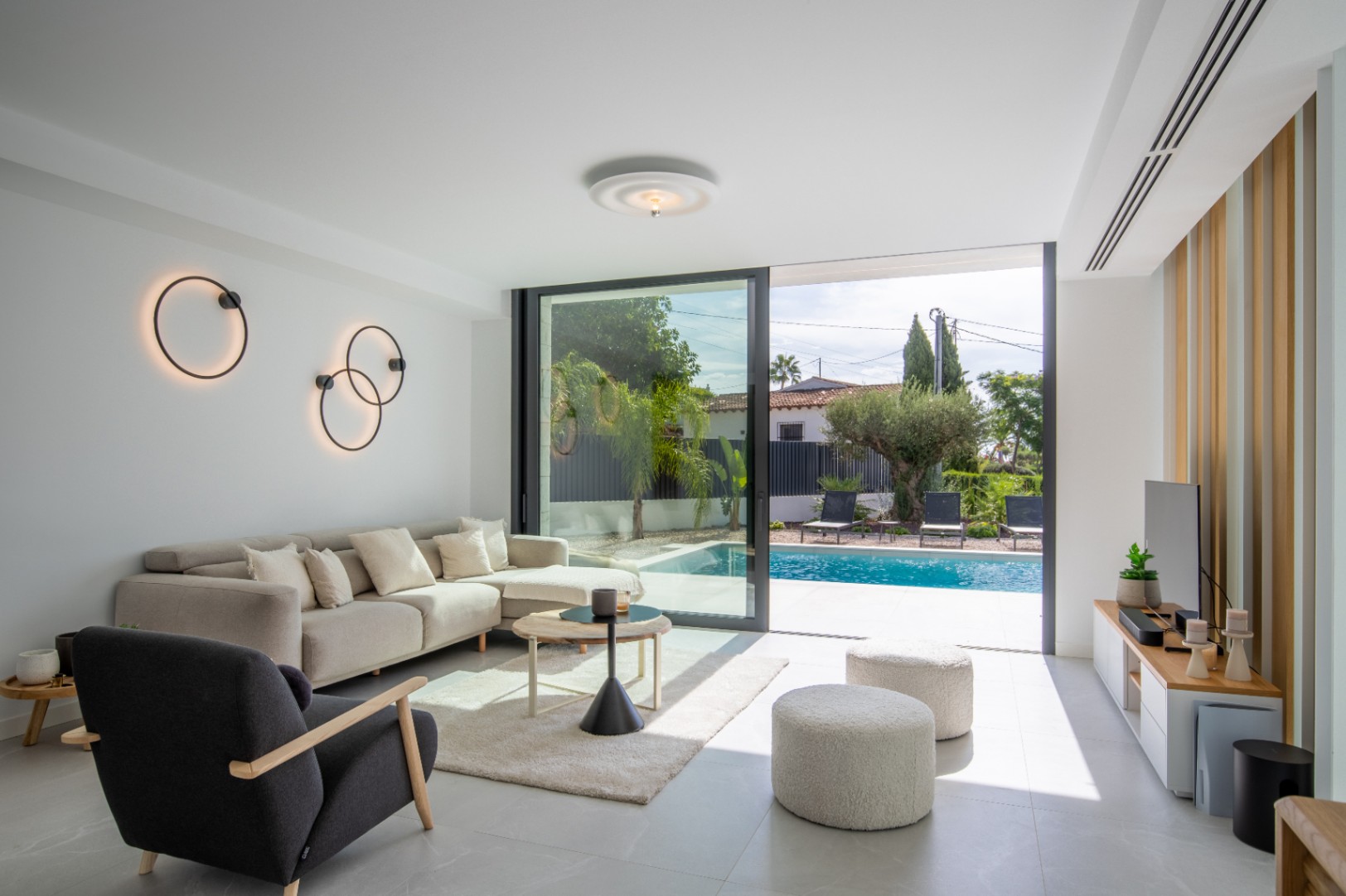 Luminoso salón con acceso directo a la piscina, decorado con apliques circulares y mobiliario moderno.
