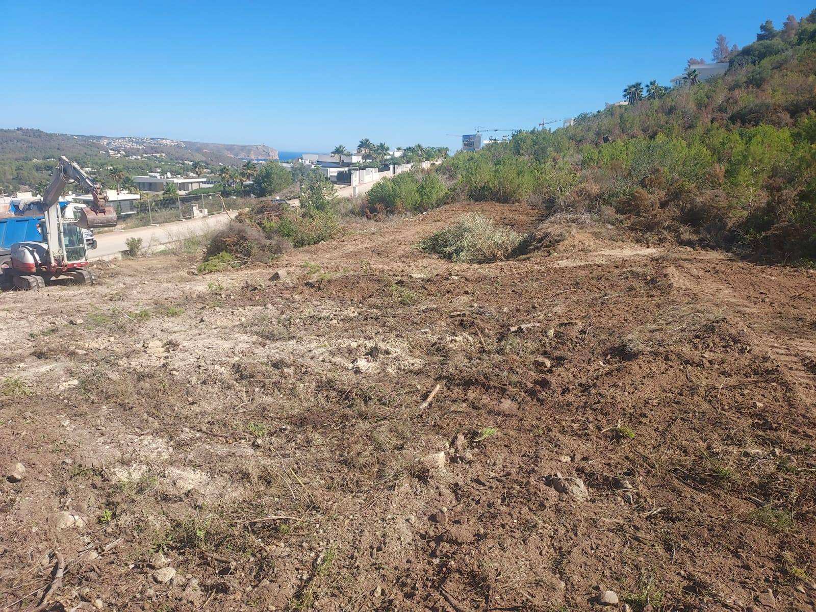 Terreno en preparación en Jávea con excavadora y vistas al mar.