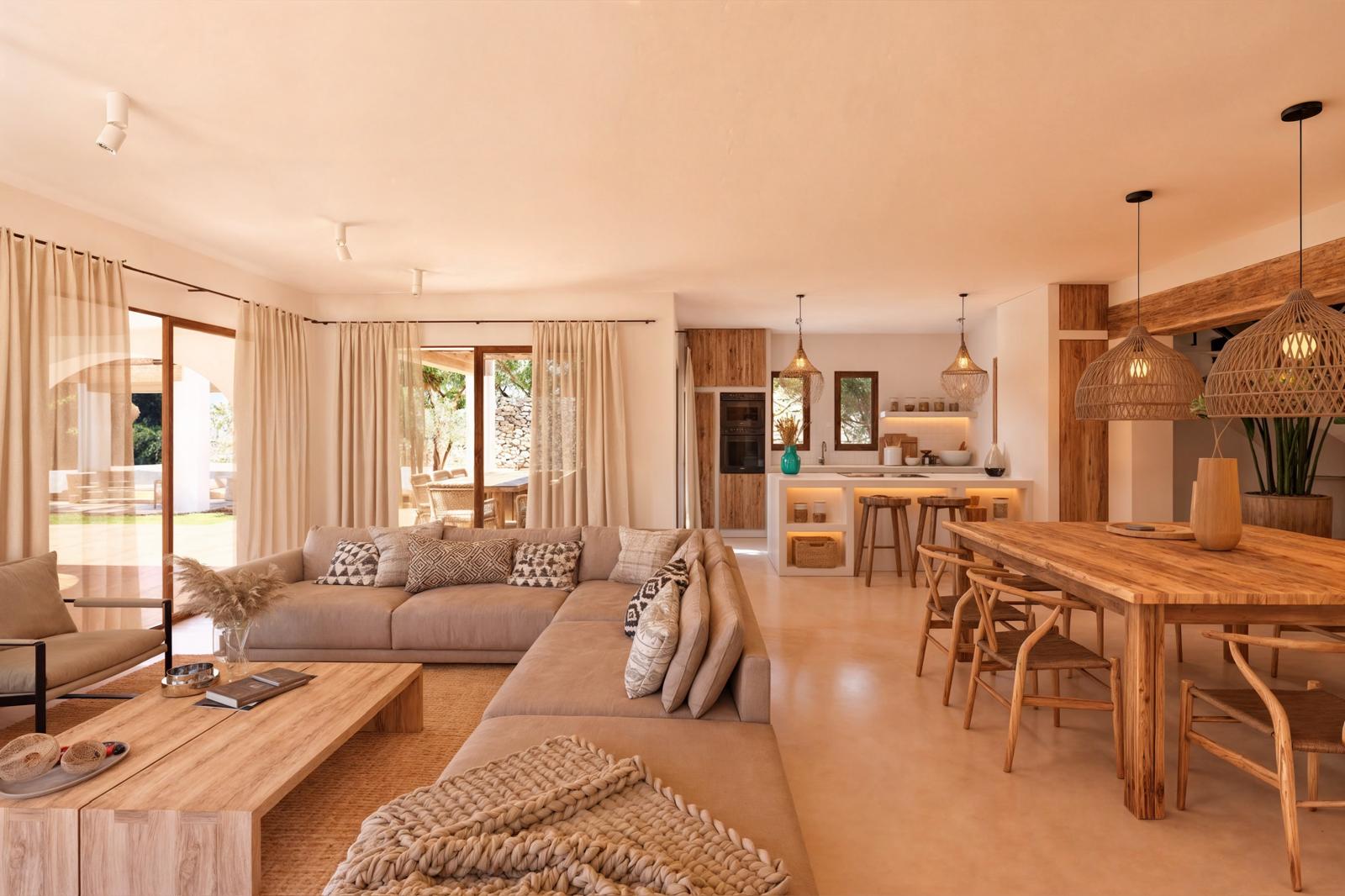 Salón-comedor de concepto abierto con mobiliario de madera natural, sofás en tonos neutros y cocina integrada con isla blanca. Destacan las lámparas de mimbre y los grandes ventanales.