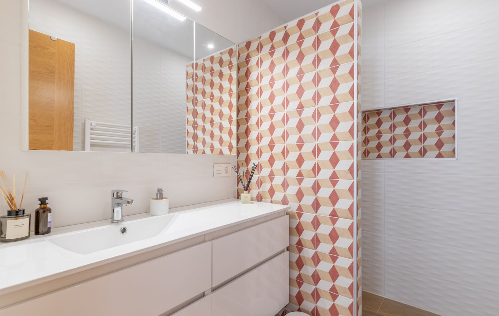 Baño moderno con mueble suspendido blanco, lavabo integrado y pared decorativa con azulejos geométricos en tonos tierra y nicho integrado.