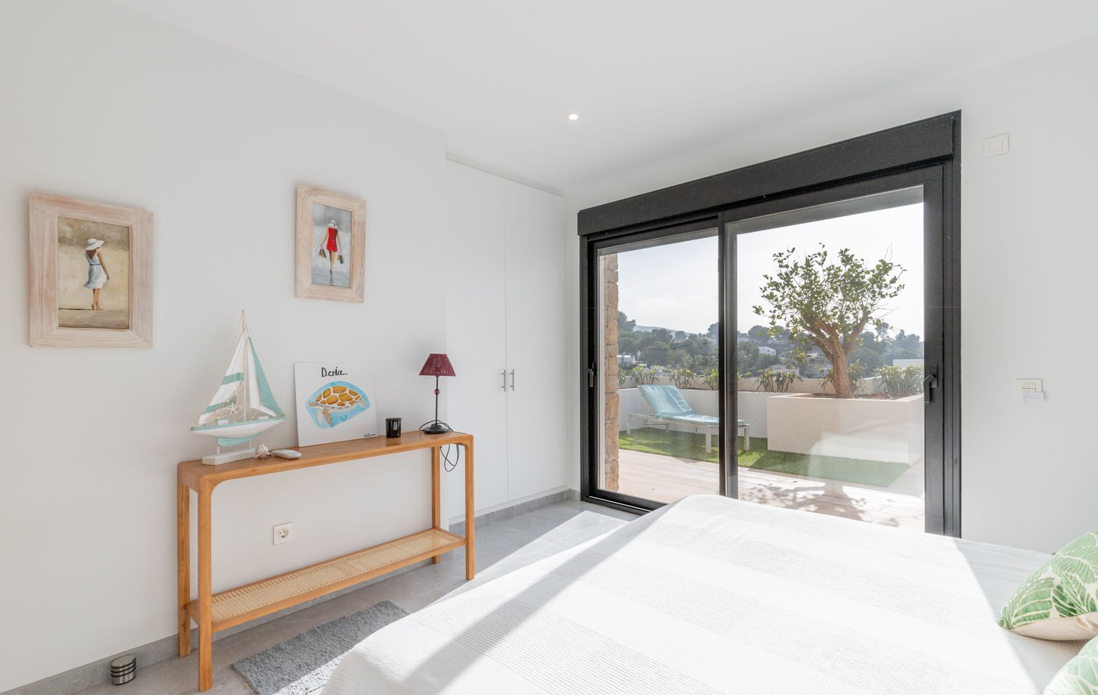 Dormitorio luminoso con armarios empotrados blancos y acceso directo a una terraza privada con césped artificial, tumbona y vistas despejadas.