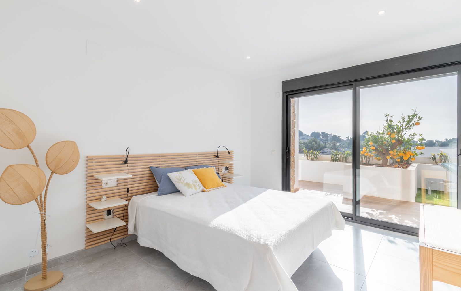 Dormitorio moderno con cabecero de listones de madera, iluminación integrada y acceso directo a la terraza privada con vistas a un jardín de cítricos.