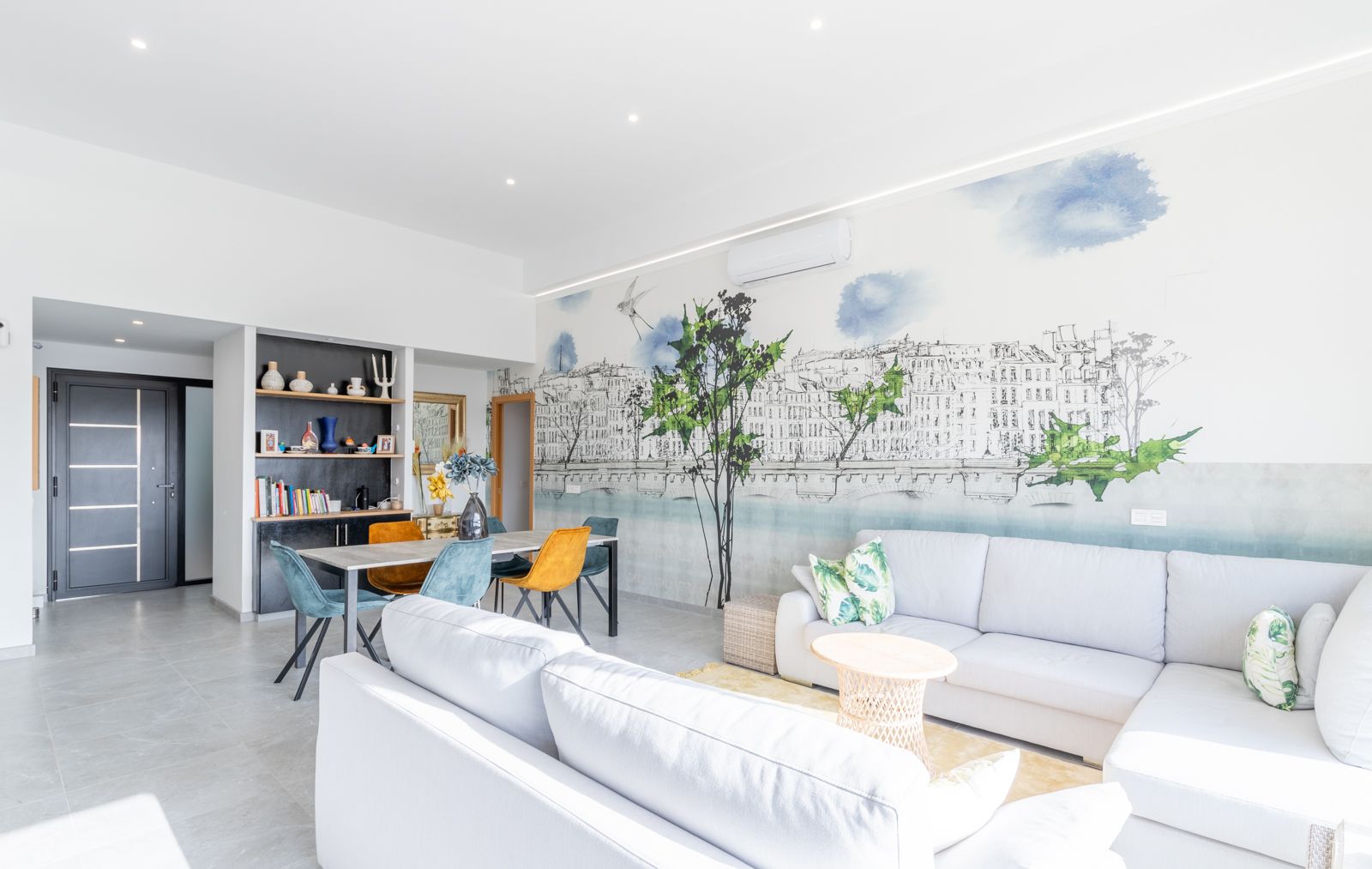 Salón comedor de concepto abierto con un gran sofá rinconero, mural artístico de diseño urbano y zona de comedor integrada con mobiliario contemporáneo.