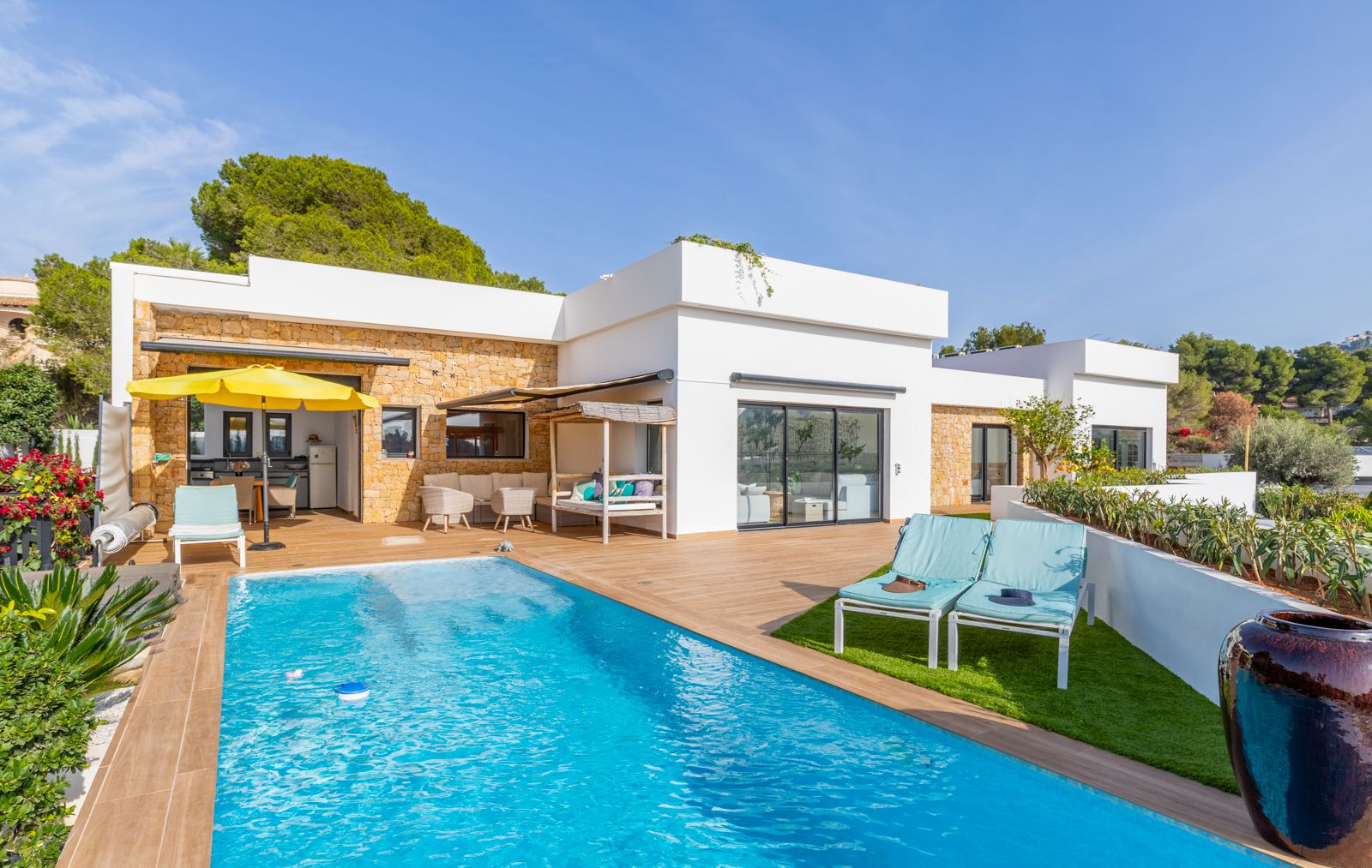 Terraza exterior con piscina, suelo de gres porcelánico imitación madera y fachada de piedra natural. Dispone de cocina de verano, solárium con césped artificial y zonas de descanso.
