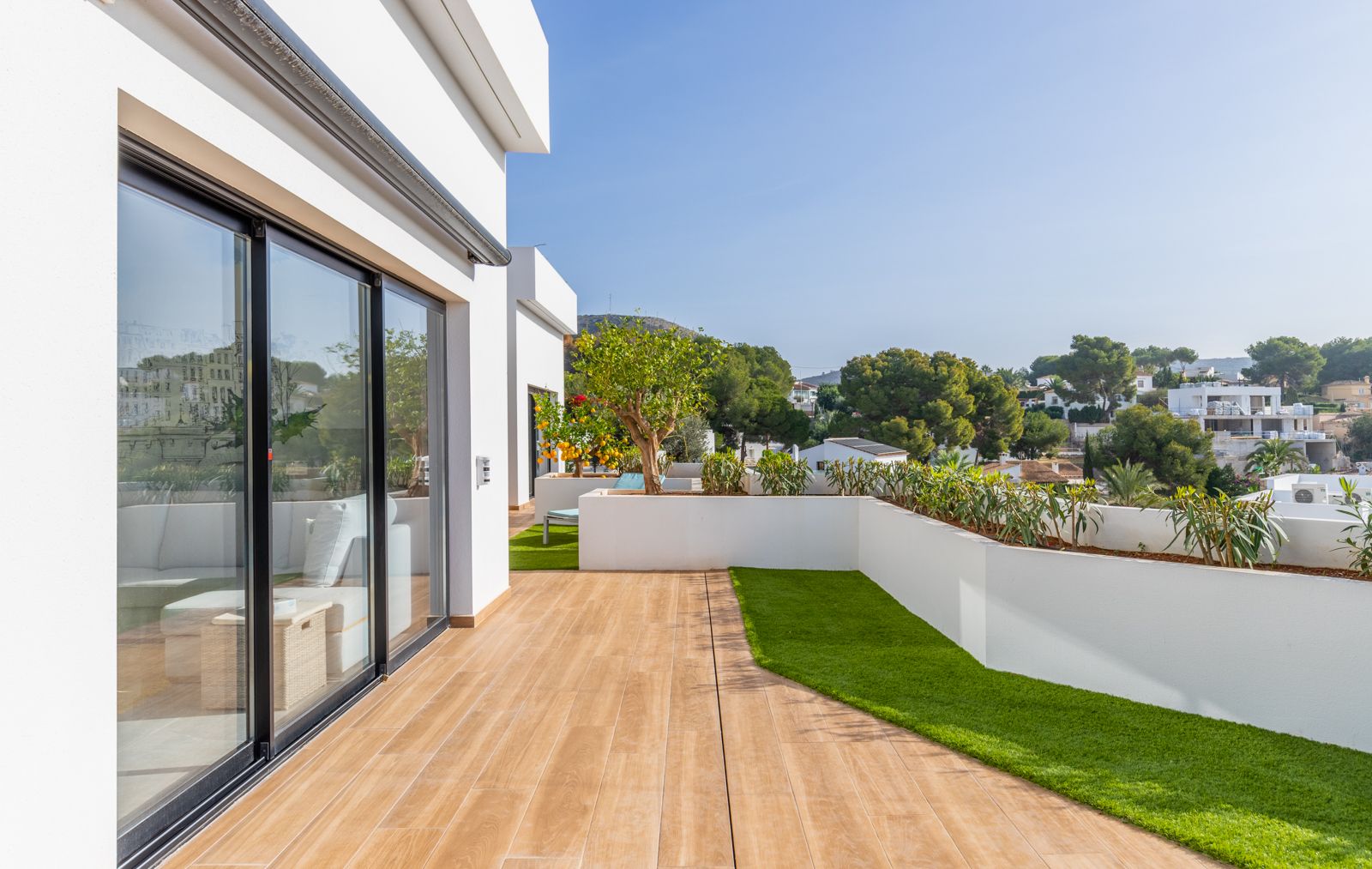 Terraza superior con pavimento porcelánico de imitación madera, zonas de césped artificial y jardineras integradas con vistas al entorno residencial.