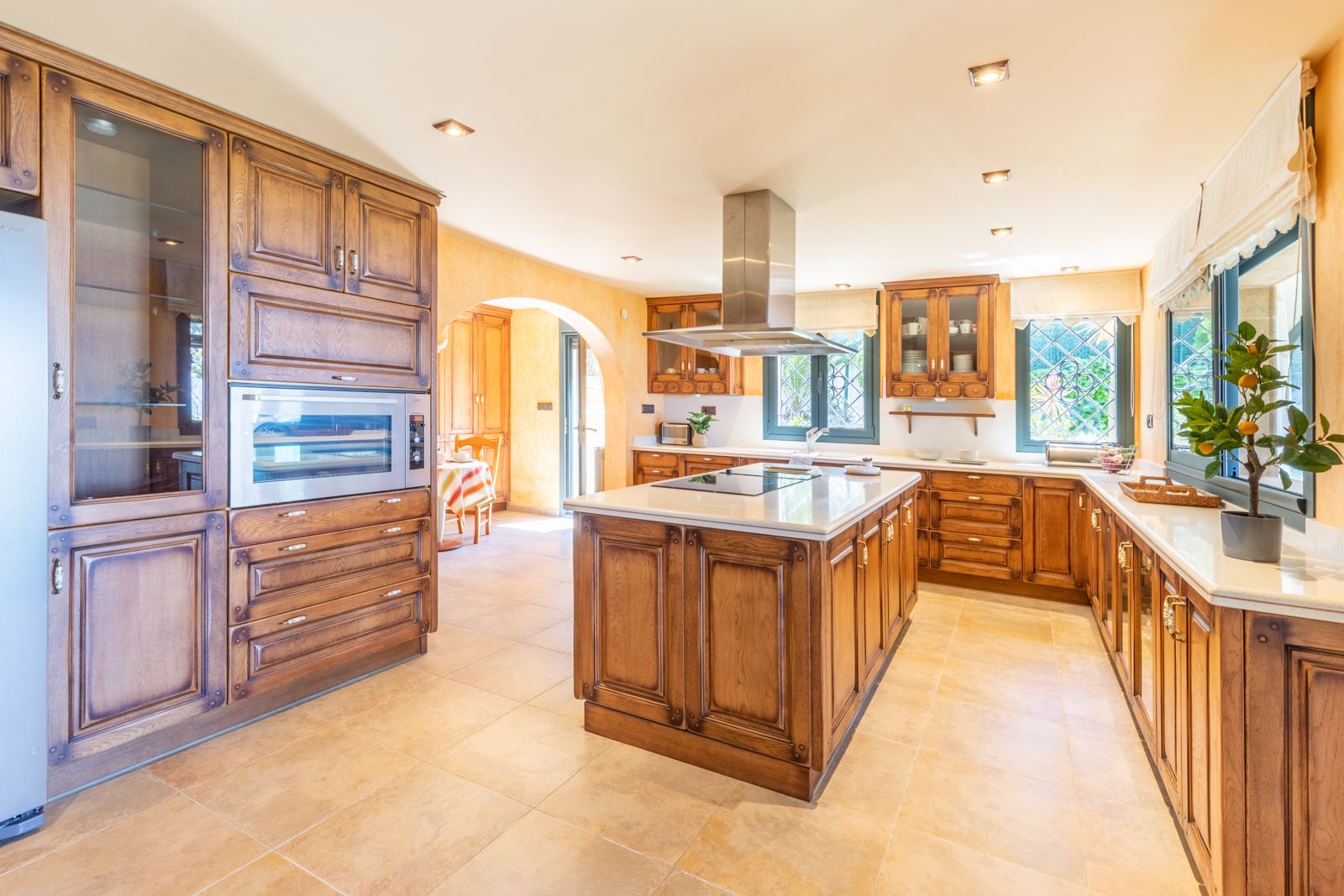 Cocina rústica con isla central, muebles de madera maciza y encimera de mármol blanco.