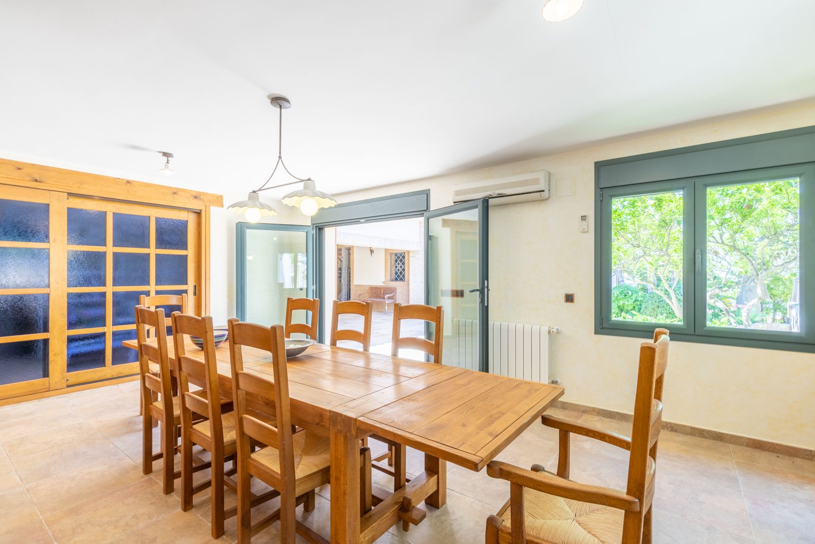 Comedor luminoso con mesa de madera maciza y sillas a juego, acceso a terraza y ventanal con vistas al jardín.