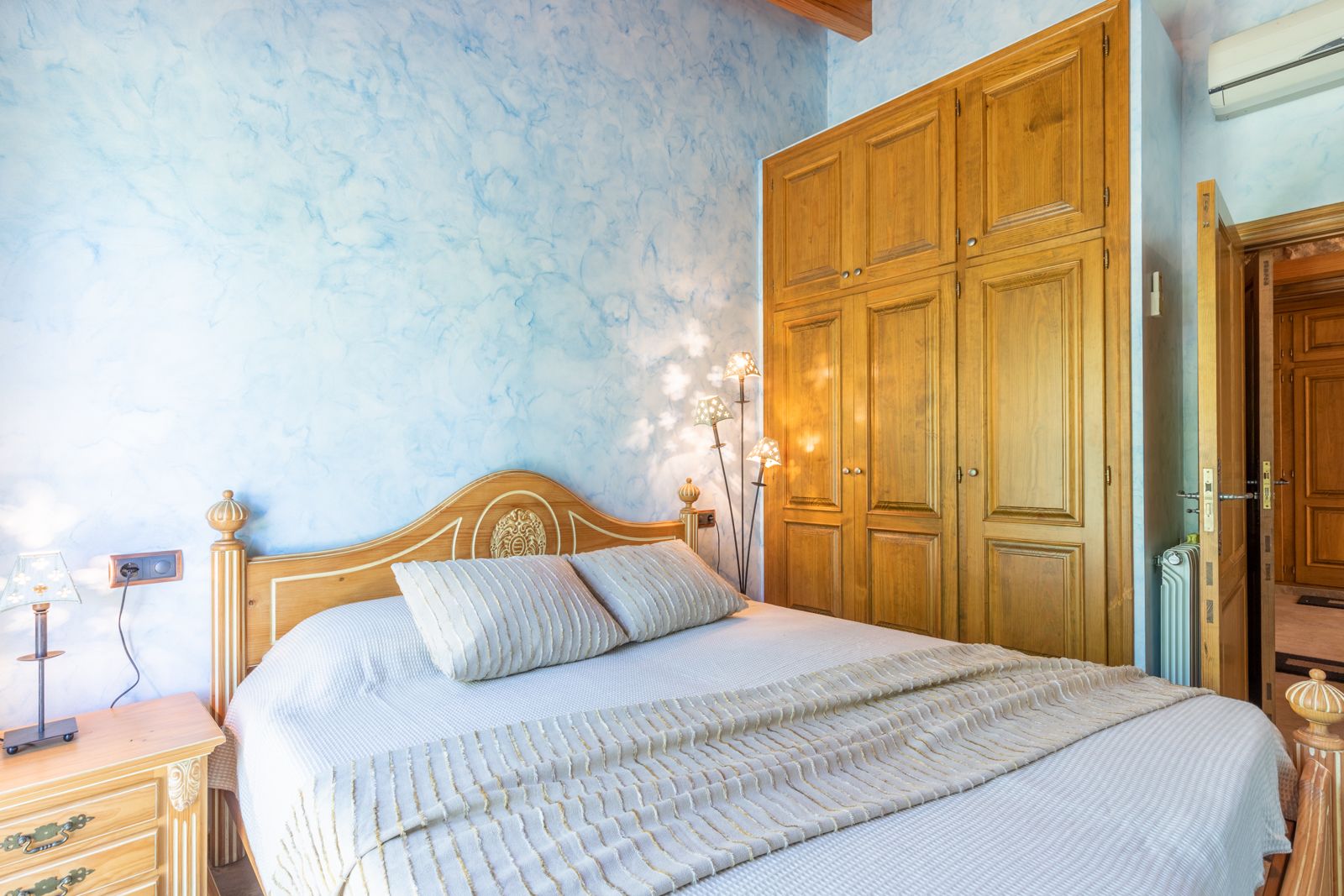 Dormitorio con pared azul texturizada, cama de madera clara y armario empotrado de madera.